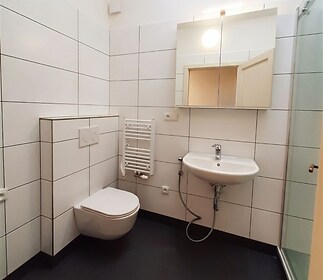 Moderní koupelna s bílými dlaždicemi, sprchovým koutem a nástěnnou toaletou. Světlý prostor s elegantním designem a účelným uspořádáním.