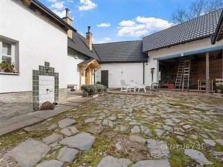 Prostorný dvůr s kamennou dlažbou poskytuje rustikální atmosféru, obklopen tradičními bílými budovami, ideální pro venkovní posezení.