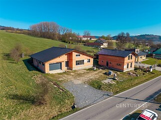 Přízemní rodinný dům s dřevěnou fasádou a velkou garáží, nacházející se na okraji klidné vesnice, nabízí moderní bydlení v přírodě.