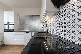 Moderní kuchyň s černobílou dlažbou, vestavěnými spotřebiči a parketovou podlahou, nabízí elegantní a funkční design.