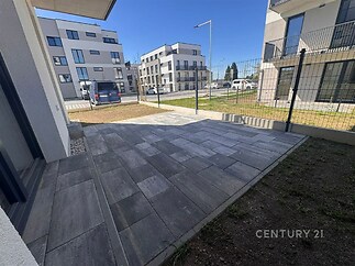Terasa s moderní dlažbou, obklopena novostavbami a oplocením, poskytuje klidné venkovní posezení v novém rezidenčním komplexu.