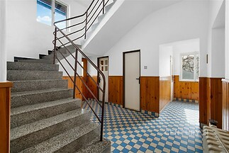 Vstupní hala s dlažbou, dřevěným obložením a schodištěm. Světlý prostor s moderní rekonstrukcí a velkými okny.