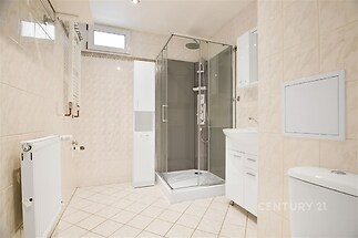 Světlá koupelna s moderní sprchou, dlažbou a světlými obklady, obsahuje praktické úložné skříňky a topný radiátor.