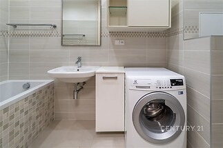 Moderní koupelna s dlažbou, vestavěnou vanou a pračkou, světlé obklady, čistý vzhled, ideální pro rekonstruovaný byt nebo dům.