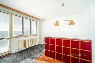 Světlá kuchyň s velkými okny, dlažbou a dřevěným barovým pultem. Jednoduchá dekorace a moderní styl nabízí příjemný prostor pro vaření.