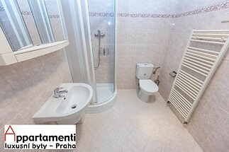 Koupelna s keramickou dlažbou, sprchovým koutem, závěsným umyvadlem a moderním topným žebříkem, vše v světlém a čistém stylu.