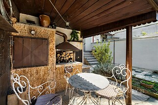 Zahradní terasa s kamennou dlažbou, stylovým venkovním posezením a krytým krbem. Klidné a útulné prostředí ideální pro relaxaci.