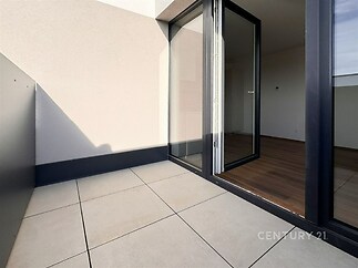 Balkon s dlažbou a velkými okny, které vedou do světlého obývacího pokoje s parketovou podlahou, moderní design a otevřený prostor.