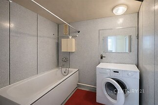 Koupelna s vanou, pračkou a vestavěnou skříňkou, s moderními panelovými stěnami a stropním osvětlením, nabízí praktický prostor v bytě.