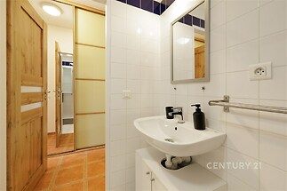 Moderní koupelna s bílými obklady a dlažbou, stylová umyvadlová skříňka a zrcadlo, dřevěné dveře dodávají teplý pocit.