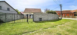 Uzavřený venkovní prostor s trávníkem, zdí a kovovou branou. Venkovský styl, klidná lokalita, ideální pro soukromí a relaxaci.