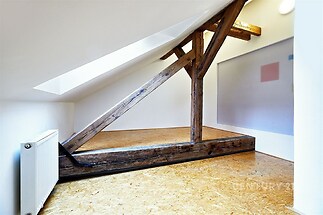 Podkrovní místnost s dřevěnými trámy, moderní OSB podlahou a střešním oknem, poskytuje světlé a útulné prostředí.