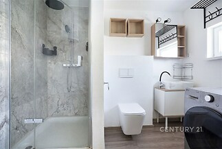 Moderní koupelna s mramorovým obkladem, sprchovým koutem a parketovou podlahou, světlé a funkční řešení s vestavěnou skříní.