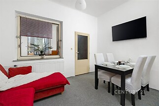 Světlá jídelna s moderním stylem, červený gauč, velká okna s výhledem, koberec na podlaze, elegantní jídelní stůl se čtyřmi židlemi.