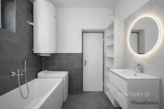 Moderní koupelna s tmavou dlažbou, stylovým kulatým zrcadlem, vestavěnou vanou a úložnými prostory.