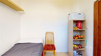 Malý pokoj s jednoduchým nábytkem, dřevěná police a židle, světlé stěny a čistý design, ideální pro minimalistické bydlení.