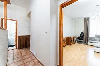 Chodba s dlažbou, vedoucí k světlému obývacímu pokoji s parketovou podlahou a velkým oknem, které poskytuje dostatek přirozeného světla