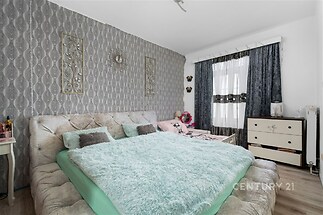 Prostorná ložnice s parketovou podlahou, stylovou tapetou a velkou postelí. Světlý interiér s moderním designem a oknem s závěsy.