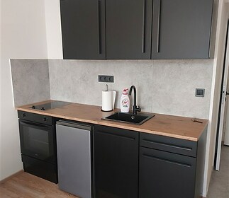 Moderní kuchyň s dřevěnou pracovní deskou, černými skříňkami a parketovou podlahou vytváří elegantní a funkční prostor.