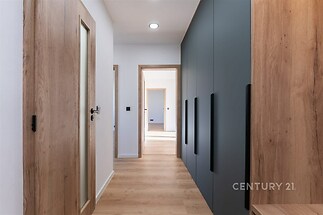 Úzká chodba s vestavěnými skříněmi, moderní dřevěné obložení a parketová podlaha, světlý prostor díky neutrálním tónům a osvětlení.