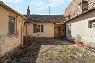 Venkovní dvůr s betonovou podlahou ve špatném stavu, obklopený staršími zdmi se známkami opotřebení, vhodný k rekonstrukci.