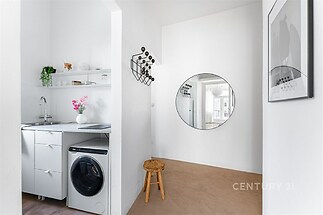 Vstupní hala s moderním stylem, světlé zdi, kulaté zrcadlo a praktická dlažba. Kuchyňský kout s vestavěnou pračkou a bílými skříňkami.