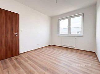 Světlý pokoj s laminátovou podlahou, velká okna a moderní styl.