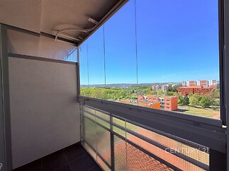 Zasklený balkon s výhledem na město, dlaždicová podlaha a moderní krytí poskytují útulný a chráněný prostor pro relaxaci.
