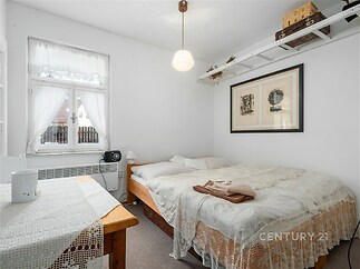 Prostorná ložnice s dřevěným stropem, světlým nábytkem a velkým oknem, které zajišťuje dostatek přirozeného světla, vytváří útulný dojem.