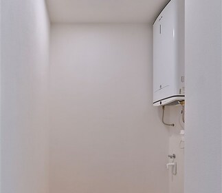 Prádelna s dřevěnou podlahou, moderní bojler a světlé stěny, ideální pro uskladnění a údržbu domácnosti.