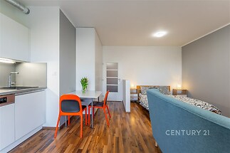 Moderní garsoniéra s parketovou podlahou, světlým nábytkem a kompaktní kuchyňskou linkou.