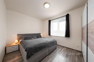 Prostorná ložnice s moderní parketovou podlahou, velkým oknem a vestavěnými skříněmi, světlý a elegantní design přidává na útulnosti.