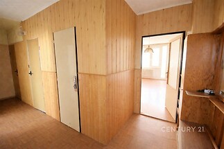 Chodba s dřevěným obložením, parketovou podlahou a vstupem do světlého obývacího pokoje, nabízející útulný a rekonstruovaný interiér.