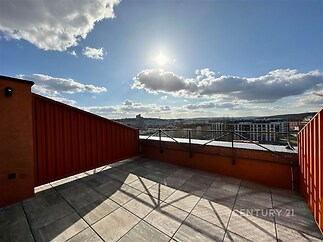 Terasa s moderní dlažbou a panoramatickým výhledem na město, výrazné kovové zábradlí, slunný prostor ideální pro relaxaci.