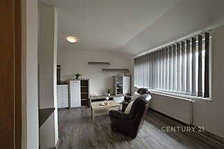 Světlý obývací pokoj s parketovou podlahou a velkými okny, moderní vestavěné skříně a elegantní dekorace přispívají k útulné atmosféře.