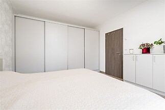 Světlá ložnice s vestavěnými skříněmi, moderní úprava a parketová podlaha, minimalistický design a prostorné úložné možnosti.