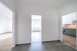 Prostorná chodba s dlažbou, vede do světlého obývacího pokoje s parketovou podlahou a moderní kuchyně s vestavěnými spotřebiči.