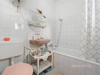 Koupelna s bílými dlaždicemi, vanou a růžovým umyvadlem. Světlý prostor s moderními prvky.