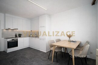 Moderní kuchyň s dlažbou a bílými skříňkami, vedle je světlý jídelní kout s dřevěným stolem a šedými židlemi.