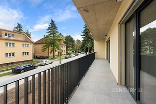 Prostorný balkon s dlažbou, moderním zábradlím a výhledem na klidnou ulici; ideální pro relaxaci a venkovní posezení.