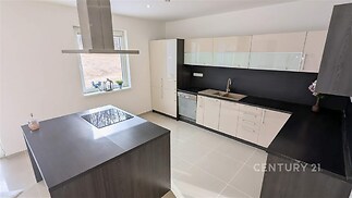 Moderní kuchyň s lesklými skříňkami, dlažbou a vestavěnými spotřebiči, světlá díky velkým oknům a minimalistickému designu.