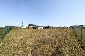 Stavební pozemek s rovinatým terénem, oplocením a blízkostí inženýrských sítí, vhodný pro výstavbu moderního rodinného domu.