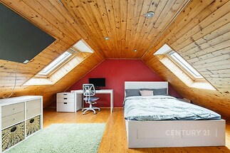 Podkrovní ložnice se dřevěným obkladem, velkými střešními okny a parketovou podlahou, moderní a světlý interiér nastavující komfortní atmosféru.