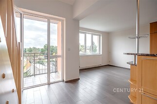 Světlý obývací pokoj s velkými okny, parketová podlaha nabízí moderní vzhled, balkon poskytuje výhled a dodatečné světlo do prostoru.