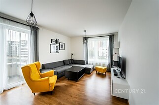 Světlý obývací pokoj s parketovou podlahou, velká okna, moderní design, pohodlná sedací souprava, žluté křeslo pro kontrast.