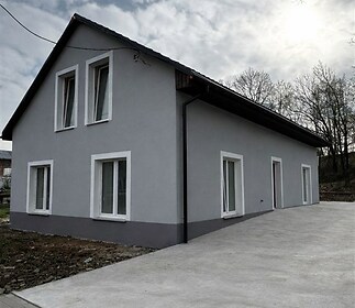 Moderní rodinný dům s šedou omítkou, nová plastová okna a prostorná příjezdová cesta, nacházející se v klidné lokalitě.