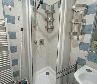 Kompaktní koupelna s rohovým sprchovým koutem, modro-bílými kachličkami a moderními kovovými doplňky, ideální pro malé prostory.