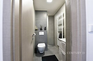 Moderní koupelna s šedou dlažbou, závěsnou toaletou a stylovým topením. Elegantní design a kvalitní materiály vytvářejí čistý vzhled.