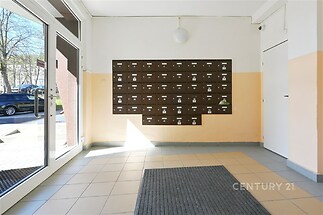 Vstupní hala bytového domu s dlažbou, poštovními schránkami a velkými okny zajišťujícími dostatek přirozeného světla.