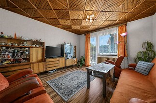Světlý obývací pokoj s dřevěným obložením stropu, parketová podlaha, velká okna, retro nábytek, pohodlné posezení v historickém stylu.